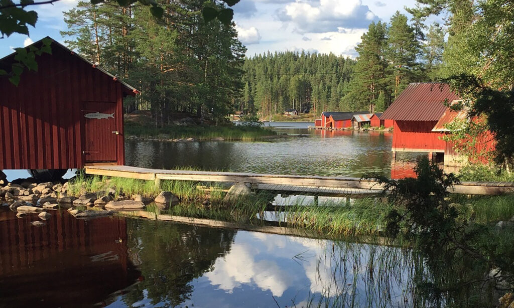 Sjön Gimmen i Dalarna. Röda sjöbodar, en brygga och skog i bakgrunden.
